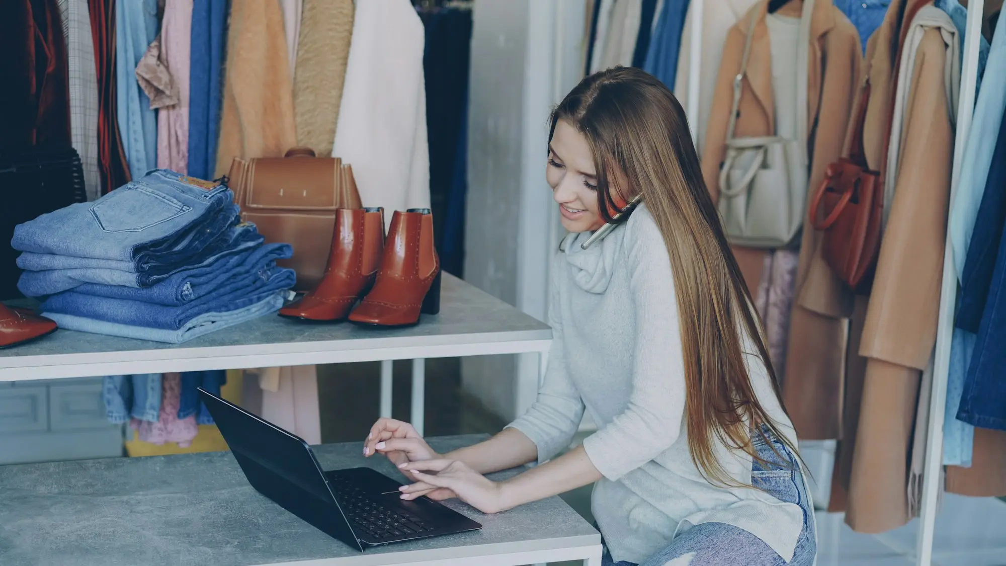 Boutique owner working on a laptop among clothing racks in her store