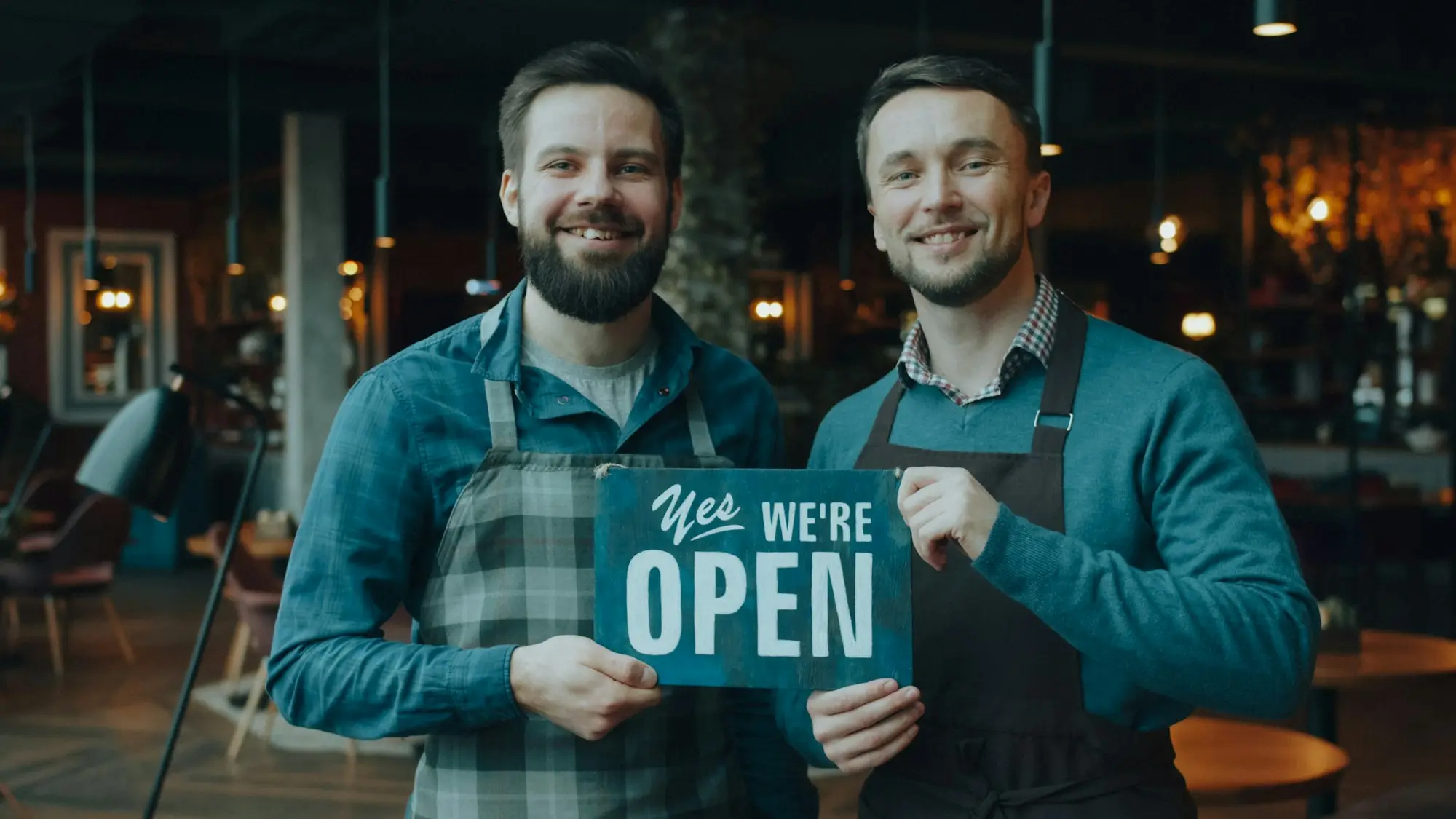 Two new business owners holding a we're open sign in their shopfront